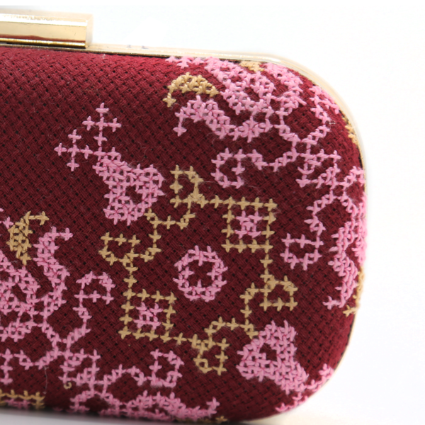 Close-up of intricate pink and gold Tatreez cross-stitch patterns on burgundy fabric evening bag.