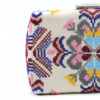 Close-up of intricate hand-embroidered Palestinian Tatreez motifs in pink, blue, and gold on a luxury cream canvas clutch.